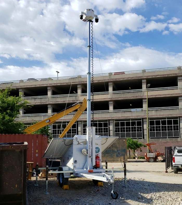 Surveillance trailer with its mast fully extended beside a multi-storey parking structure, cameras positioned above roof level.